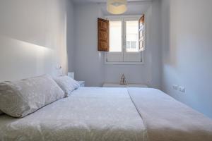 een witte slaapkamer met een groot bed met een raam bij Puerta Real Centro Apartment in Granada