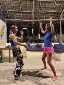 dos mujeres bailando en la arena en la playa en Juani beach bungalows en Kilindoni