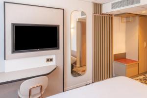 a bedroom with a bed and a tv and a mirror at Brit Hotel Nantes La Beaujoire Parc Expo in Nantes