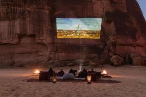 a group of people sitting in front of a wall with a tv at Caravan by Habitas AlUla in Al Ula
