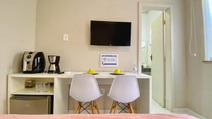 a kitchen with two white stools and a table with a tv at Kalug - Suíte CASAL com AR, SMART TV e WI-FI 200mbps in Ilhéus