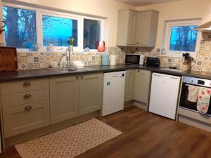 a kitchen with white cabinets and white appliances at Woodpecker Cottage in Carnguwch