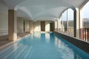 an indoor pool with blue water in a building with windows at Abrigo da Montanha Hotel Rural in Sabugueiro