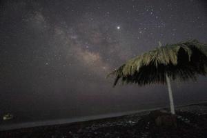 uma noite estrelada com um guarda-sol de palha na praia em Ktima Tzaneti - Coastal Farmhouse em Lacónia