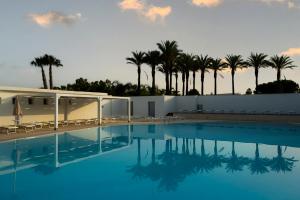 a swimming pool with a building and palm trees at Nicolaus Club Magna Grecia in Metaponto