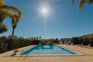 a swimming pool with the sun in the sky at Baglio Calia in Mazara del Vallo