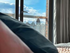 a person laying on a bed looking out a window at Apartament Waterlane w oknami na rzekę - Marina View in Gdańsk