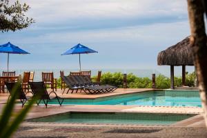 a swimming pool with chairs and blue umbrellas at Hotel Pontal de Ubu in Anchieta