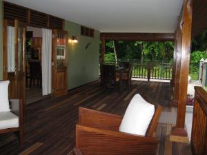 een woonkamer met houten vloeren en een veranda met stoelen bij Casa Verde in Grand'Anse Praslin