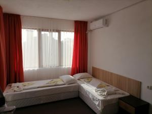 two beds in a room with a window with red curtains at Ivet Guest Rooms - Obzor in Obzor