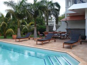 a swimming pool with chairs and a table and palm trees at Residence Lestridents in Flic-en-Flac