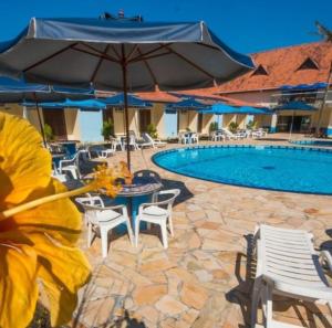 a pool with tables and chairs and an umbrella at Rota do Sol Praia Hotel in Guaratuba