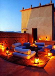 a patio with blue pillows and lights and a building at Hotel Riad Le Petit Prince in Merzouga