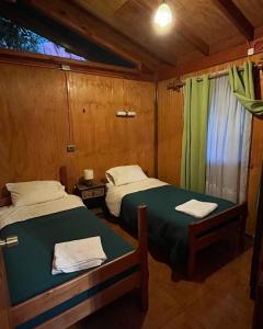 two beds in a small room with green sheets at Cabaña Antu-Meli, Liquiñe in Liquiñe