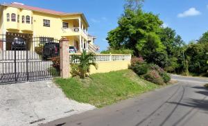 a yellow house with a fence on a street at Royal Escape in Anse La Raye