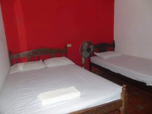two beds in a room with red walls and a fan at Hostal Vacaciones Nicas in León