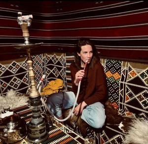 a woman sitting on a bed brushing her teeth at Happy Bedouin House Petra in Al Ḩayy
