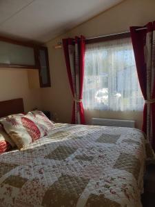 - une chambre avec un lit doté de rideaux rouges et d'une fenêtre dans l'établissement La Chanterie Agréable Mobil-Home Résidentiel Normand, à Saint-Pair-sur-Mer