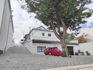a red car parked next to a tree on a street at Hall 92 Quartos com WC em moradia com piscina A-das-Lebres Loures in Loures