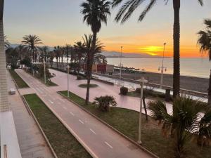 Málaga paraíso frente al mar في مالقة: شارع فيه نخيل وشاطئ عند الغروب