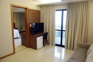 a hotel room with a tv and a couch and a bed at Pituba Praiamar Hotel in Salvador