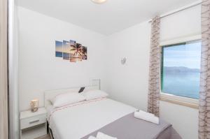 a white bedroom with a bed and a window at Apartment Paradise in Postira