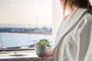 uma mulher segurando um copo de café branco em uma janela em Byssus Suites em Siracusa