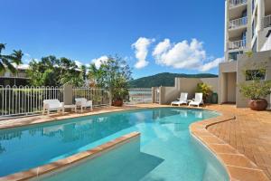 a swimming pool with chairs and a building at at Whitsunday Vista Holiday Apartments in Airlie Beach