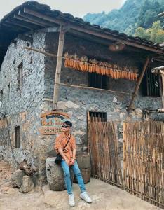 a man sitting on a rock in front of a building at Minh Khang Homestay - Làng đá cổ Khuổi Ky in Cao Bằng