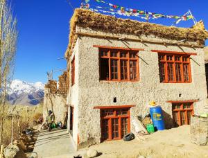 een gebouw met rode ramen en een man die buiten zit bij Likir Pottery Homestay - Likir Village - Sham Valley in Leh