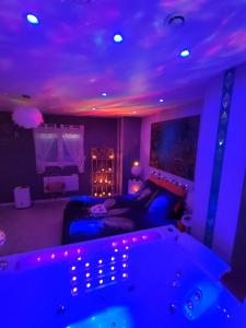 Habitación con cama y bañera con luces moradas. en Loft avec Baignoire SPA LÉcrin Romantique, en Ochancourt