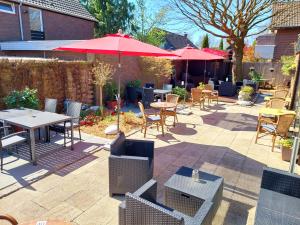 een patio met tafels en stoelen en rode parasols bij Hotel Rosmarin in Bad Zwischenahn