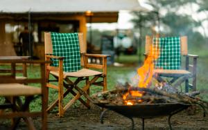 zwei Stühle und eine Feuerstelle im Hof in der Unterkunft Gnu Mara River Camp in Serengeti-Savanne