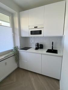 een witte keuken met een wastafel en een magnetron bij DOCK 12 - Exklusives Cityapartment in Bremerhaven