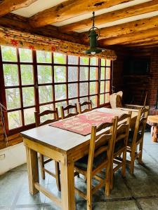 een houten tafel en stoelen in een kamer met ramen bij Cabaña en la costa del Lago Futalaufquen - Parque Nacional Los Alerces in Esquel