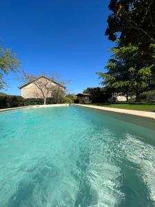a pool of blue water with a house in the background at Le Jasmin in Montcaret