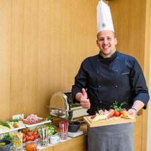 a chef giving a thumbs up while holding a board of food at Hotel Bono in Budva