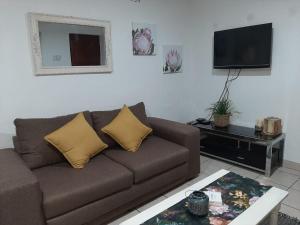 a living room with a brown couch and a flat screen tv at The Cottage in Grahamstown