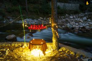 a table sitting next to a river with lights at LivingStone Backwater Resort Tirthan Valley in Banjār