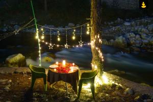 a table with candles and lights on it next to a tree at LivingStone Backwater Resort Tirthan Valley in Banjār