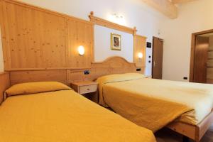 two beds in a hotel room with yellow sheets at Hotel Majorka in Andalo
