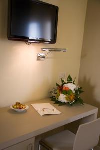 una mesa con un tazón de flores y una TV en la pared en San Francesco Hotel en Loreto