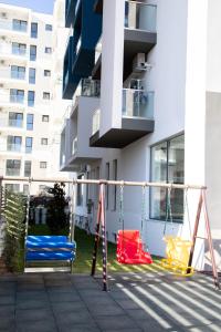une aire de jeux avec balançoires en face d'un bâtiment dans l'établissement Turquoise Apartment Nord10 - Pool n Parking, à Mamaia