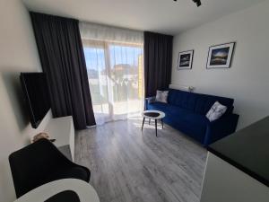 a living room with a blue couch and a large window at Loft Apartamenty w Sarbinowie in Sarbinowo