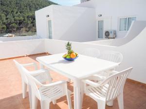 una mesa blanca y sillas con un bol de fruta. en Apartamentos Cala Llonga en Cala Llonga