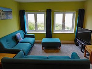 a living room with two blue couches and two windows at Bryn Melyn Apartments in Barmouth
