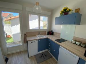 une cuisine avec des placards bleus, un évier et une fenêtre dans l'établissement « Heures claires » logement de charme avec parking, à Saint-Georges-de-Didonne