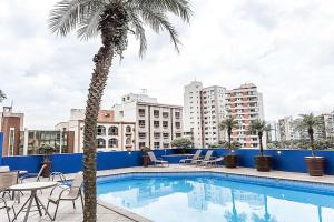 a swimming pool with a palm tree and buildings at Comfort Suítes Vitória in Vitória