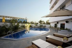 a swimming pool with chairs and an umbrella next to a building at Lemon Tree Hotel Hinjewadi Pune in Pune