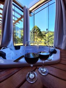 Dois copos de vinho numa mesa com uma banheira em Recanto da Pedra Chalé em São Bento do Sapucaí